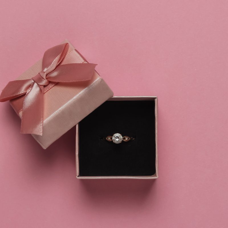 Gift box and engagement gold ring with diamond on pink pastel background. Wedding, romantic concept. Jewelry. Top view. Flat lay